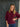 Woman wearing a maroon sweater and blue jeans standing against a dark wooden door.