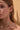 Close-up of a woman wearing gold earrings and a necklace against a beige background
