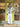 A woman stands in front of a storefront doorway wearing a white and navy striped button-up shirt with white wide-leg pants and tan sandals. The door behind her is bright yellow-green, and clothing is visible inside the shop windows.