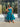 A woman wearing a sleeveless green and blue floral midi dress stands in front of a clothing store window displaying other garments.