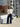 Woman standing in front of a store with floral decorations, wearing a white sweater and dark jeans.