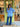 Woman standing outside a store with a green door, wearing a blue striped shirt and jeans.