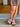 Person wearing a brown skirt and colorful sandals on a wooden floor.