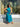 A woman wearing a sleeveless halter midi dress with a blue and green abstract print, posing in front of a clothing store window.