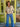 Woman wearing a beige cardigan and blue jeans standing in front of a green door.