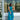 A woman wearing a sleeveless teal and blue floral midi dress stands in front of a clothing store window display.