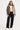 Woman wearing a beige quilted jacket, white shirt, and black pants on a white background