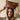 Woman holding a brown leather handbag above her head against a beige background