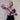 Woman in a purple striped shirt holding a black bag against a light stone wall.