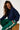 Woman wearing a navy sweatshirt and green tracksuit with white stripes, sitting on a wooden block against a white background.