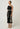 Elodie One Shoulder Embroidery Dress Black side view highlighting the striking one-shoulder silhouette and embroidered hemline.