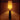 A table lamp with a glowing warm yellow cylindrical shade and a dark tapered base, shown lit against a dim brown background.