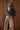 Woman wearing a blue denim blouse and beige pants against a wooden paneled wall.