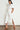 Full length side profile view of a model wearing the Legacy Dress in elm white, showcasing the midi length silhouette, button-through styling with antique brass buttons, and side slit detail.