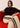 Woman sitting on a red couch wearing a striped sweater and beige pants with black stripes.