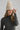 Woman wearing a beige knit beanie with a pom-pom on a plain background