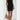 Person wearing a black dress with white trim holding a tan handbag on a white background