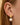 Gold earring with a pearl drop worn by a person with brown hair.