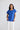 Close-up front view of a model wearing the Percy Top in Cobalt paired with white trousers.