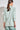 Back view of the Refine Jacket in pistachio green, highlighting the relaxed fit, shoulder pads for soft structure, and 3/4 length sleeves with ruched detail.