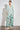 Full length view of a model wearing the Refine Jacket in pistachio green paired with printed pants, showcasing a relaxed fit and softly structured silhouette.