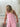 Reversible Tiki overalls shown on the solid soft washed pink reverse side featuring front pocket detail and adjustable straps.