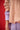 Xena Pullover Tan close-up detail view highlighting the sleeve design and layered styling over a red background.