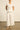 Full length front view of a model wearing the Yonder Top in porcelain white, featuring a 100% ramie relaxed silhouette, square neckline, and scalloped lace trims.